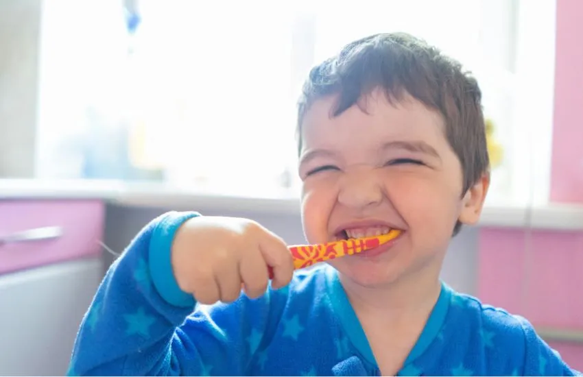 Niño pequeño cepillándose los dientes en el baño con la ayuda de su madre, fomentando la higiene bucal infantil desde casa.
